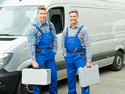 Zwei Handwerker in blauen Overalls stehen neben einem Lieferwagen und halten Werkzeugkoffer.